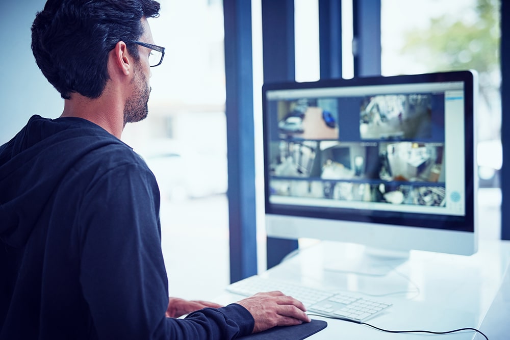 Cropped shot of a young man watching security footage on his com